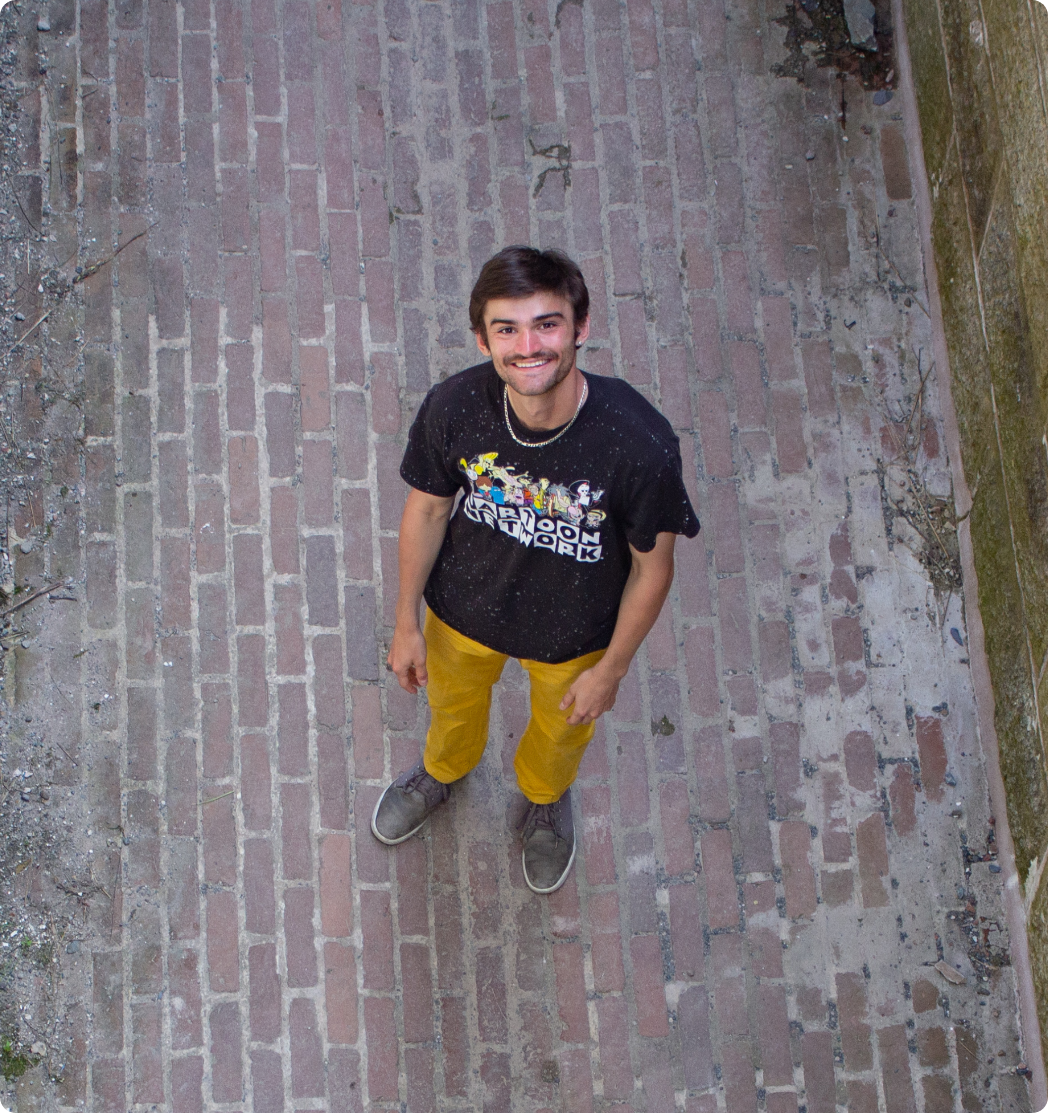 Photograph of Sam Giustizia smiling, taken from a top down perspective while he's in some kind of outdoor concrete room